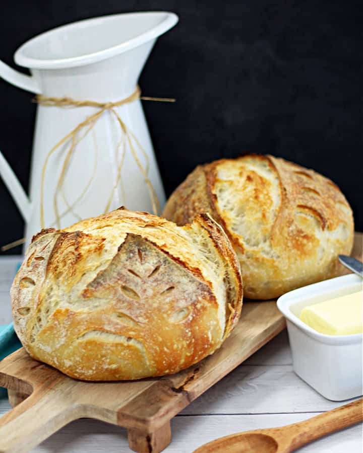 picture of two sourdough loaves on a wooden cutting board with a white container of butter