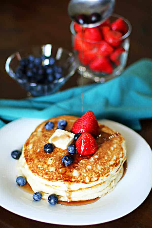 three large sourdough discard pancakes on a white plate with blueberries, strawberries and maple syrup