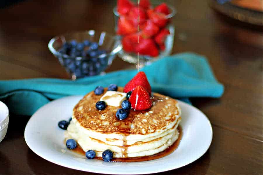 three large sourdough discard pancakes on a white plate with blueberries, strawberries and maple syrup