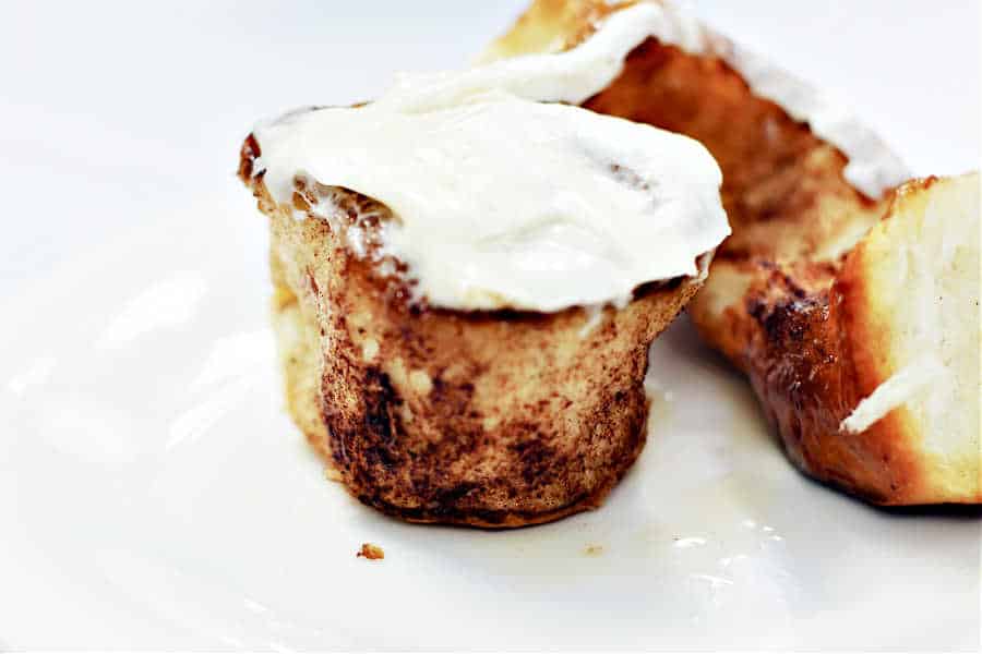 Cinnamon bun torn open with center exposed and cream cheese icing on top