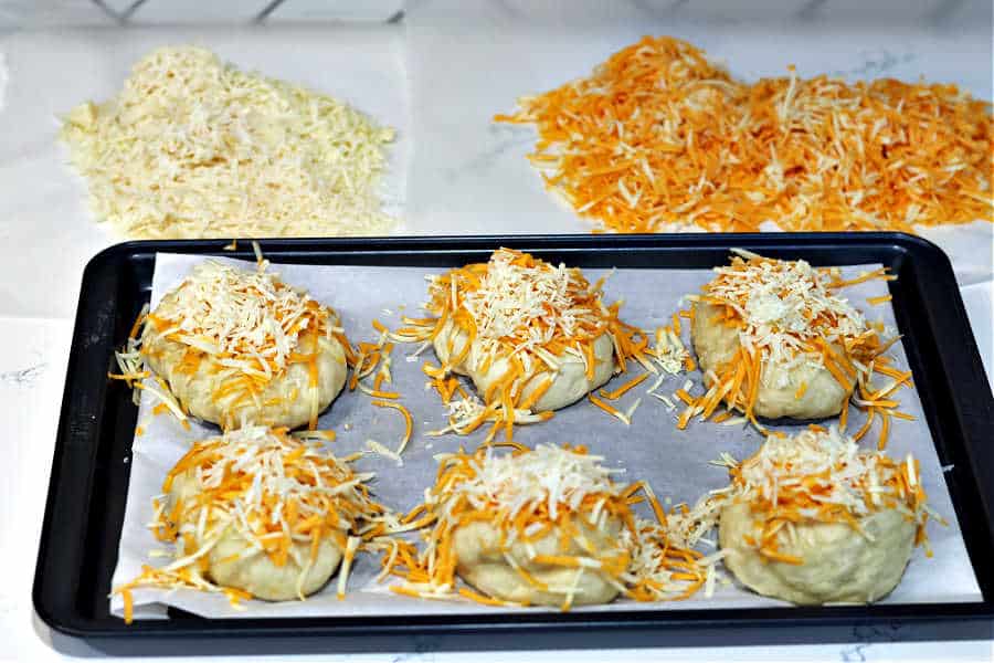 homemade bagels on a baking sheet covered in cheese, ready to bake