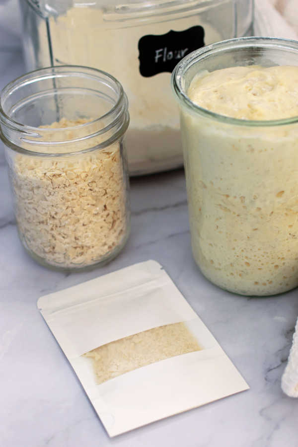 picture of flower in a jar, fresh sourdough starter, a jar of dehydrated starter and an envelope with a window filled with dehydrated starter