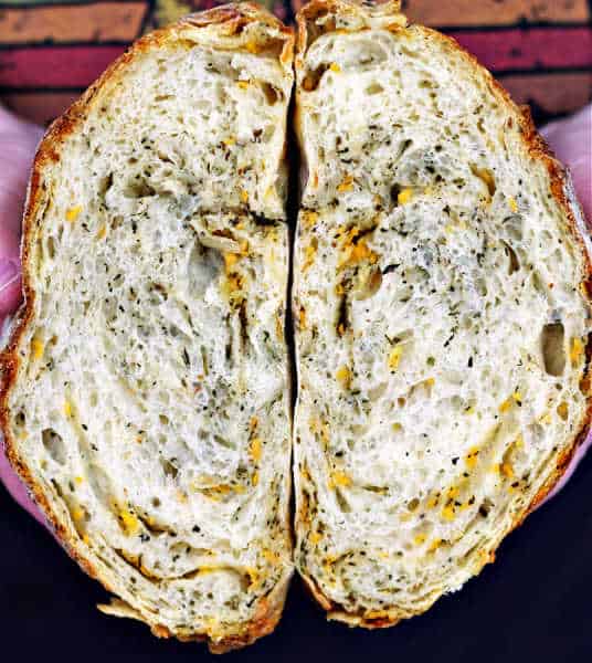 two hands holding a cut in half loaf of Italian Herb and Cheese Sourdough Artisan Bread