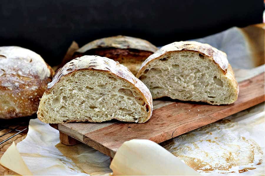 sourdough boule cut in half with both pieces placed on a brown wooden cutting board surrounded by other loaves