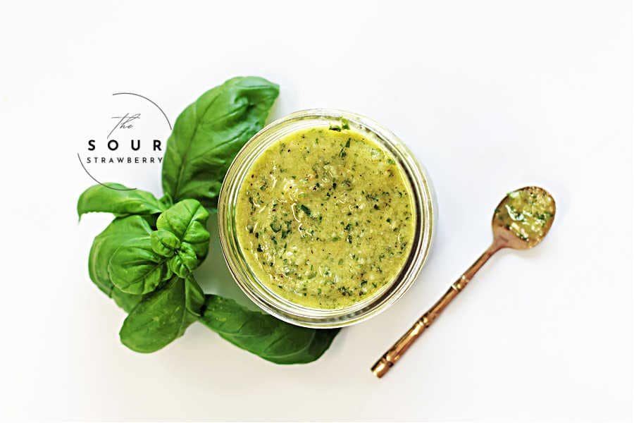 Homemade basil pesto in a glass jar, surrounded by fresh basil leaves and a gold spoon with pesto on a clean white background. This vibrant green sauce, made with fresh basil, garlic, Parmesan cheese, and olive oil, is perfect for pasta, sandwiches, or dipping. Ideal for a quick and easy 5-minute pesto recipe.